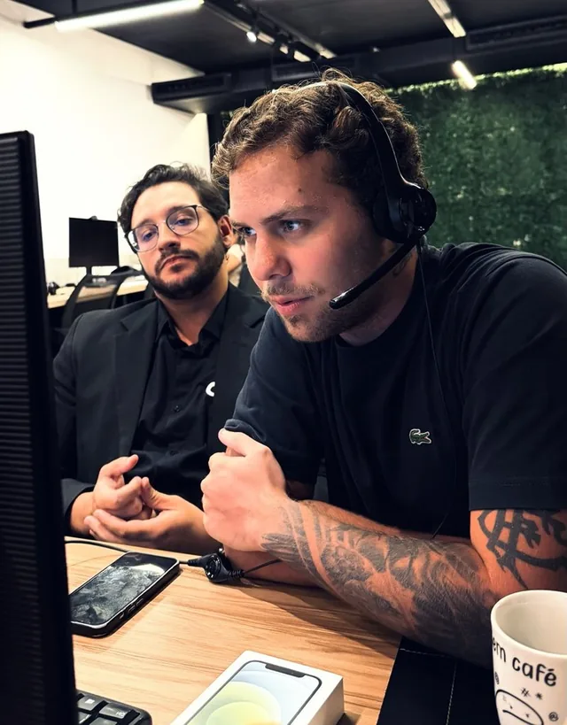 Dois profissionais da Avizz trabalhando juntos numa estação, um deles com headset de atendimento.